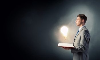 Businessman with book in hands. Businessman holding opened book with glass glowing light bulb