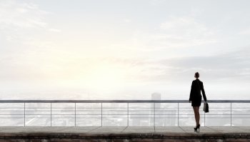 Back view of businesswoman standing on roof looking at city. On top of business