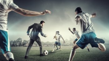 Businessman play ball. Young businessman in suit playing football with players outdoors