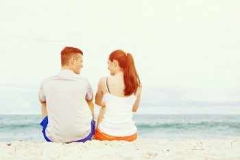 Young couple looking at each other while sitting on beach. Young couple looking at each other while sitting together on beach