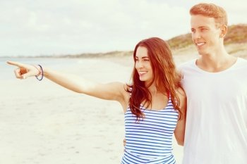 Happy young man and woman couple together walking on a beach. Happy senior man and woman couple together walking and pointing on a deserted beach