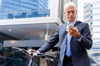 Successful businessman riding bicycle. Successful businessman in suit riding bicycle and holding mobile phone