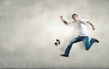 Young man in casual jumping to hit the ball. Football fan