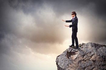 Businessman in blindfold. Image of businessman in blindfold standing on edge of mountain