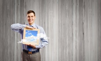 Businessman with frame. Young smiling businessman holding wooden frame with sky picture