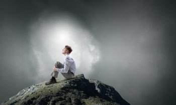 Isolated to find inspiration. Young thoughtful businessman sitting alone on rock top 
