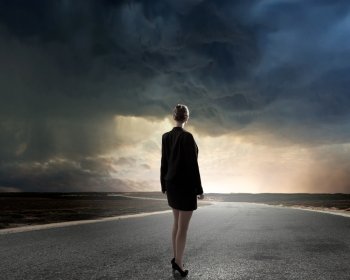 At the start of long way. Back view of businesswoman standing on road and looking far away