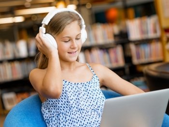A teenage girl with headphones sitting in a library. Reading and listening 