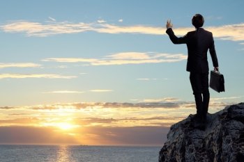 Businessman on top of hill. Image of young businessman standing on top of hill