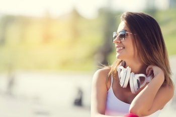 Teenager girl having time in outdoors. Attractive brunette girl in summer park enjoying daytime wearing headphones