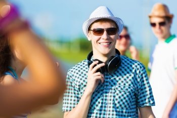 Young man with headphones. Image of young man with friends at background. Summer vacation