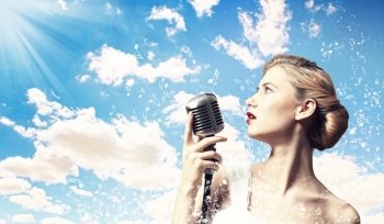 Female blonde singer. Image of female blonde singer holding microphone against clouds background