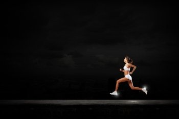 At full speed. Young woman athlete running fast on dark background 