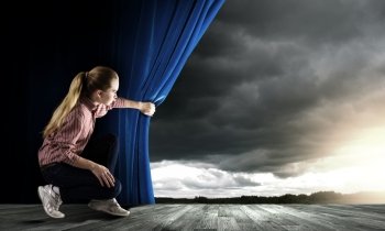 Woman looking out from curtain. Young woman in casual opening blue curtain and looking at sky