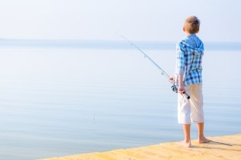 Boy in blue shirt standing on a pie. Boy in blue shirt standing on a pier with a fishing rod by the sea
