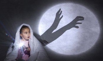 Children nightmare. Cute girl in bed under blanket with flash light