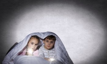 Children’s nightmares. Children sitting in bed under blanket with flashlights