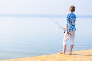 Boy in blue shirt standing on a pie. Boy in blue shirt standing on a pier with a fishing rod by the sea