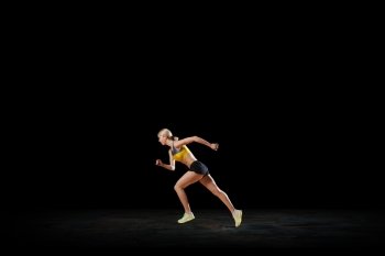 At full speed. Young woman athlete running fast on dark background 