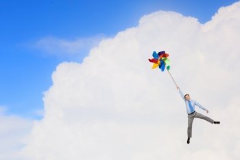 Free and careless. Young happy businessman flying in sky on colorful windmill