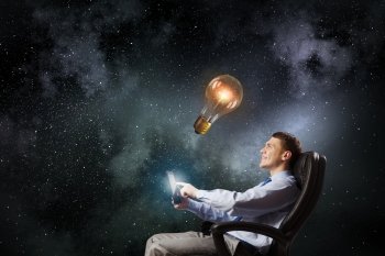 Businessman with tablet. Young businessman in armchair using tablet pc looking at glass lightbulb