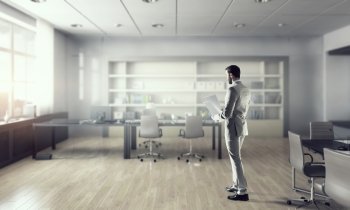 Businessman in modern office mixed media. Young elegant businessman in office thinking over busines
