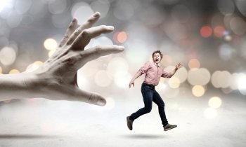Running from hand. Young man trying to run away from big male hand