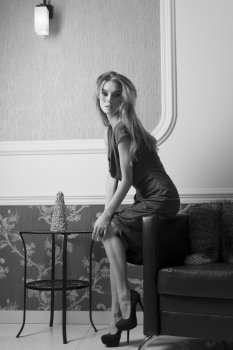 sensual girl with shiny blue dress and heels posing in elegant ambient with fur on leather sofa.image in black and white