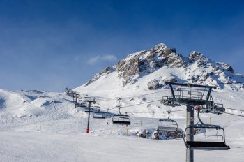 Ski lift in mountains at winter. Alpine winter mountain landscape. French Alps covered with snow in sunny day. Val-d'Isere, Alps, France