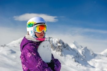 Young woman with snowboard in ski goggles outdoors with French Alps covered with snow at background. Val-d'Isere, France