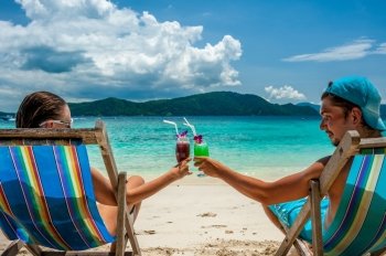 Couple in loungers clinking their glasses on a tropical beach at Thailand