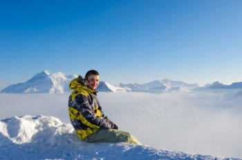 Alpine winter mountain landscape with man sitting above low clouds. French Alps covered with snow in sunny day. Val-d'Isere, France