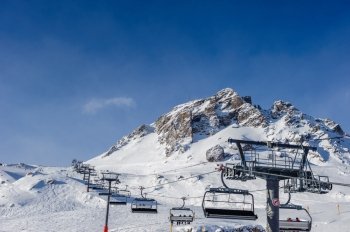 Ski lift in mountains at winter. Alpine winter mountain landscape. French Alps covered with snow in sunny day. Val-d'Isere, Alps, France