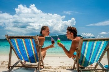 Couple in loungers clinking their glasses on a tropical beach at Thailand