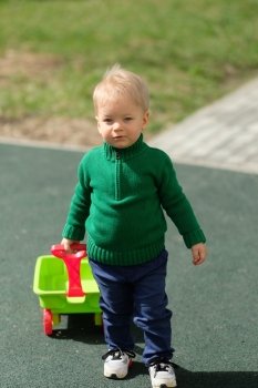 Portrait of toddler child outdoors. One year old baby boy wearing green sweater at playground