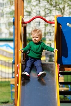 Portrait of toddler child outdoors. One year old baby boy wearing green sweater at playground slide