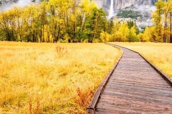 Meadow with boardwalk in Yosemite National Park Valley with Yosemite Falls at cloudy autumn morning. Low clouds lay in the valley. California, USA.