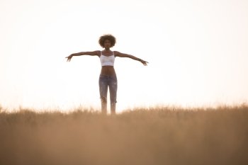 Young beautiful black girl laughs and dances outdoors in a meadow during sunset
