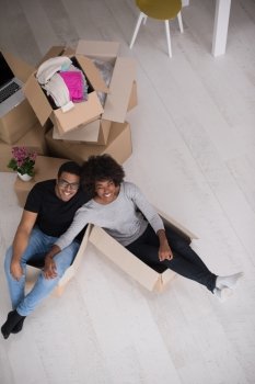 African American couple sitting in a box playing with packing material, having fun after moving in new home