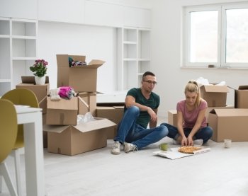 happy young couple have a pizza lunch break on the floor after moving into a new home with boxes around them