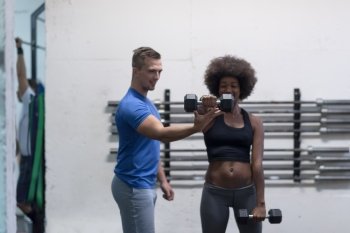 young beautiful African American woman doing bicep curls with fitness trainer in a gym
