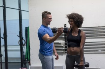 young beautiful African American woman doing bicep curls with fitness trainer in a gym