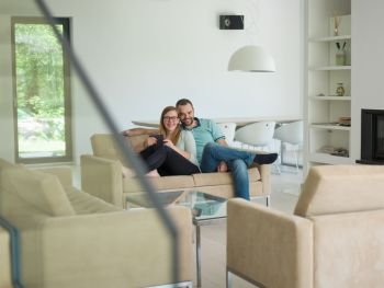 Young couple relaxes on the sofa in the luxury living room, using a tablet and remote control