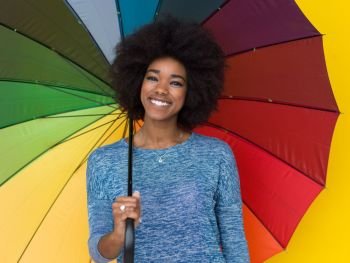 Portrait of young beautiful african american woman holding a colorful umbrella isolated on a Yellow background