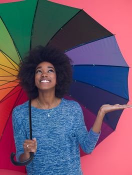 Portrait of young beautiful african american woman holding a colorful umbrella isolated on a Pink background