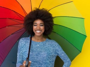 Portrait of young beautiful african american woman holding a colorful umbrella isolated on a Yellow background