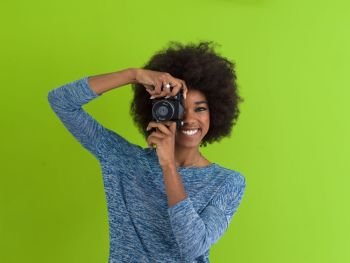portrait of a smiling pretty african american girl taking photo on a retro camera isolated over green background