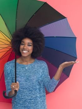 Portrait of young beautiful african american woman holding a colorful umbrella isolated on a Pink background