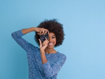portrait of a smiling pretty african american girl taking photo on a retro camera isolated over blue background
