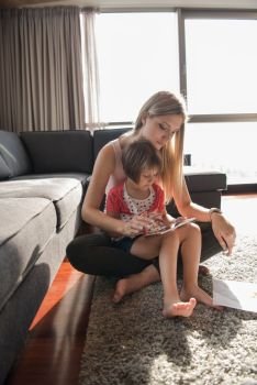 Beautiful young mother and her cute little daughter  using a tablet and smiling, sitting on the floor at home